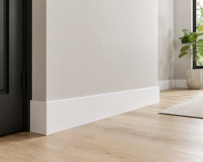 Close-up of a white baseboard in a room with a window and plant.